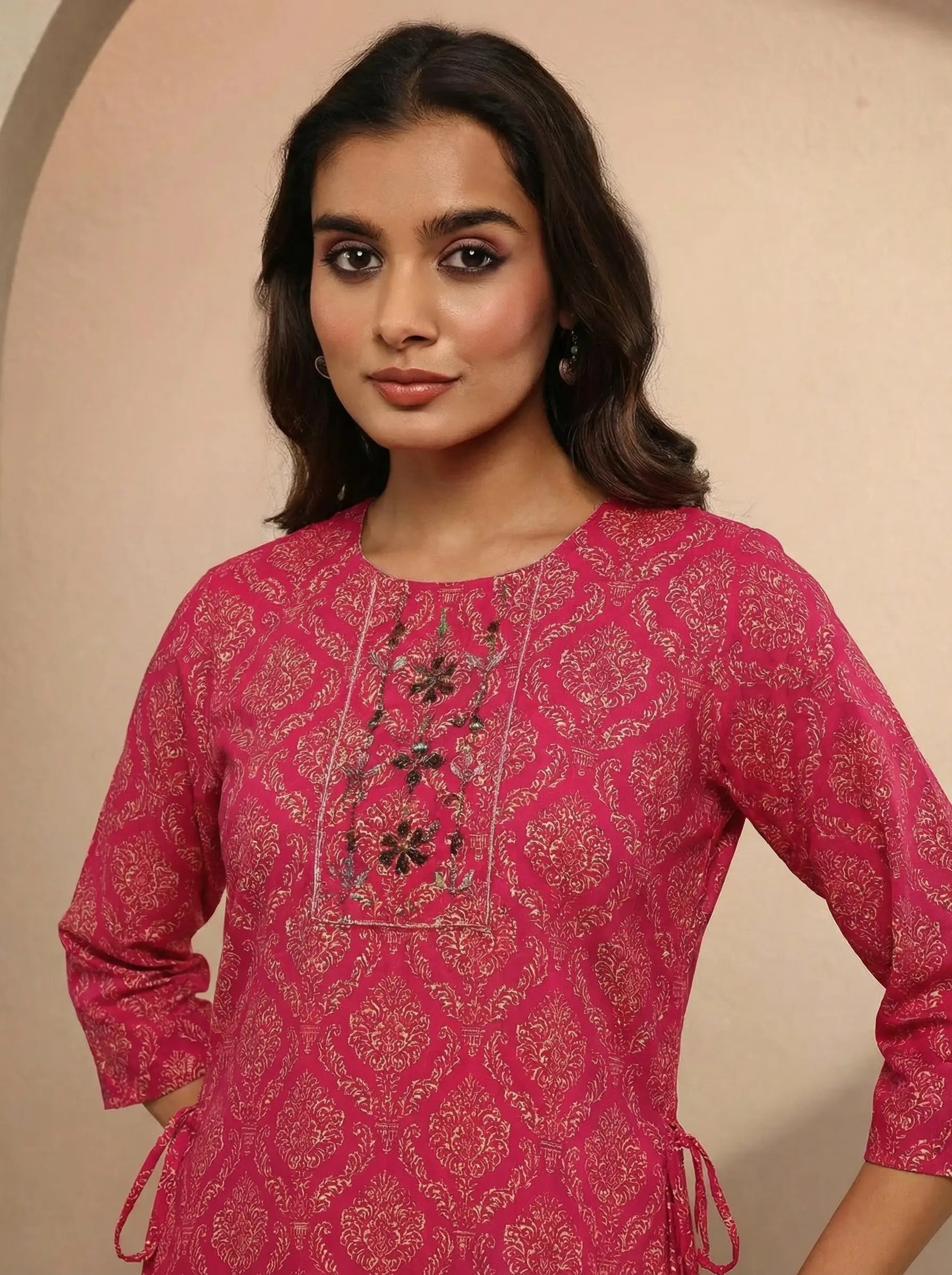 Woman wearing a pink embroidered traditional outfit against a beige background